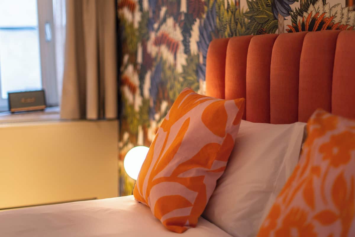 A bed with orange and white patterned pillows, a tufted headboard, and a window with curtains.