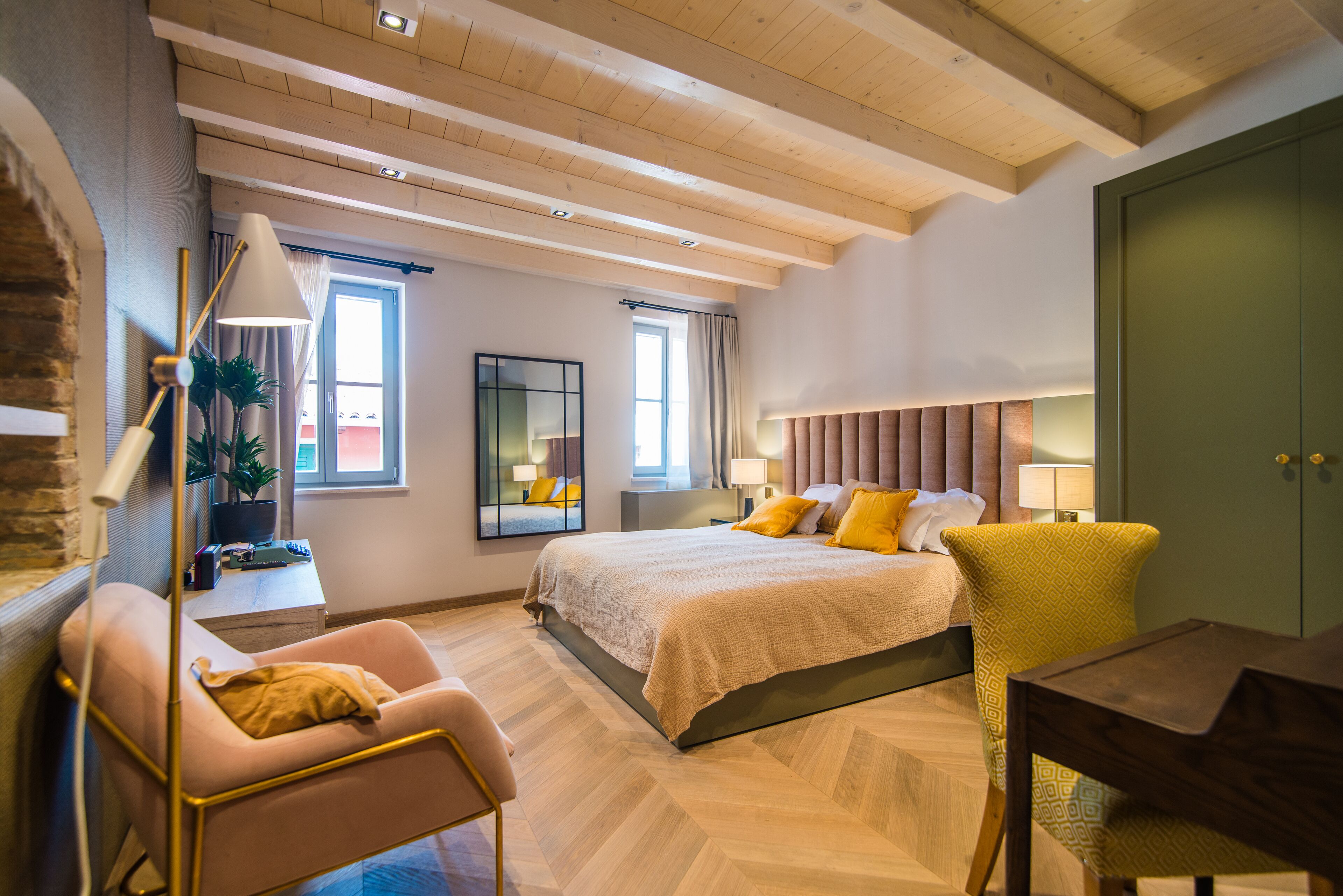 Un dormitorio moderno con una cama grande, un escritorio y una silla. Hay ventanas y un espejo en la pared.