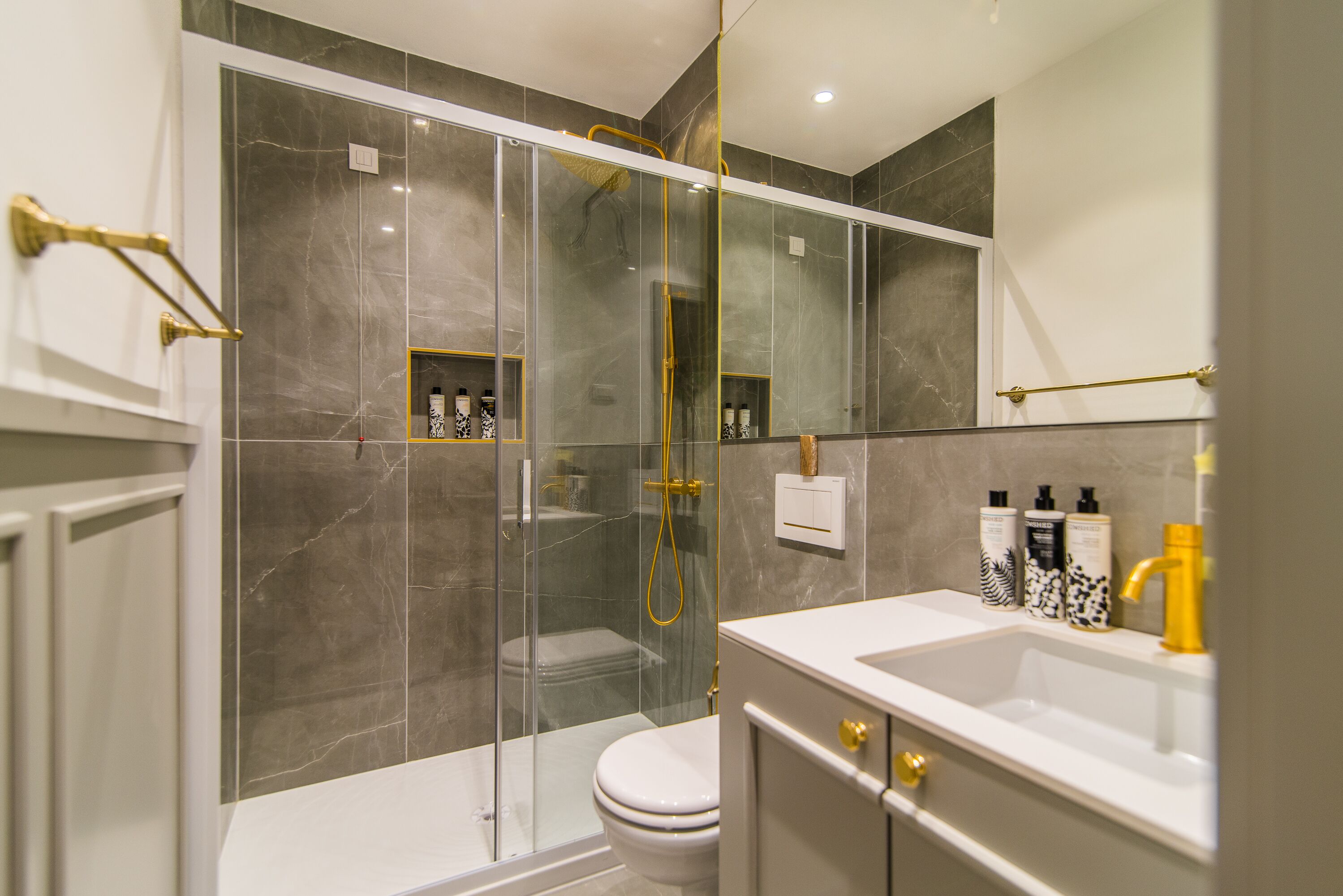 A modern bathroom with a glass-enclosed shower, a white toilet, and a vanity with a sink and mirror.