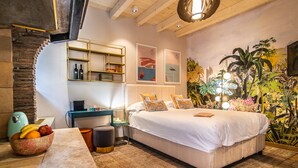 A bedroom with a bed, a nightstand, a bowl of fruit, a lamp, and a mural of a tropical scene. - The Melegran (Rovinj)