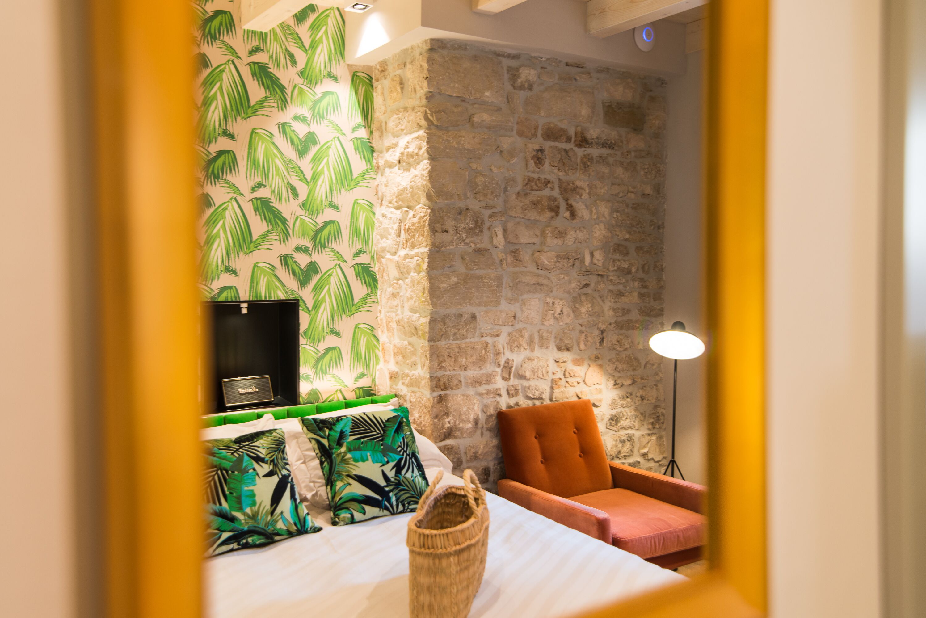 Una habitación con una cama, una silla, una lámpara y una pared con un diseño de hojas.