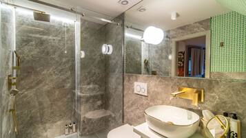Een moderne badkamer met een douchecabine van glas, een witte wastafel met gouden accenten en een spiegel met een groene, gepatteerde lijst.