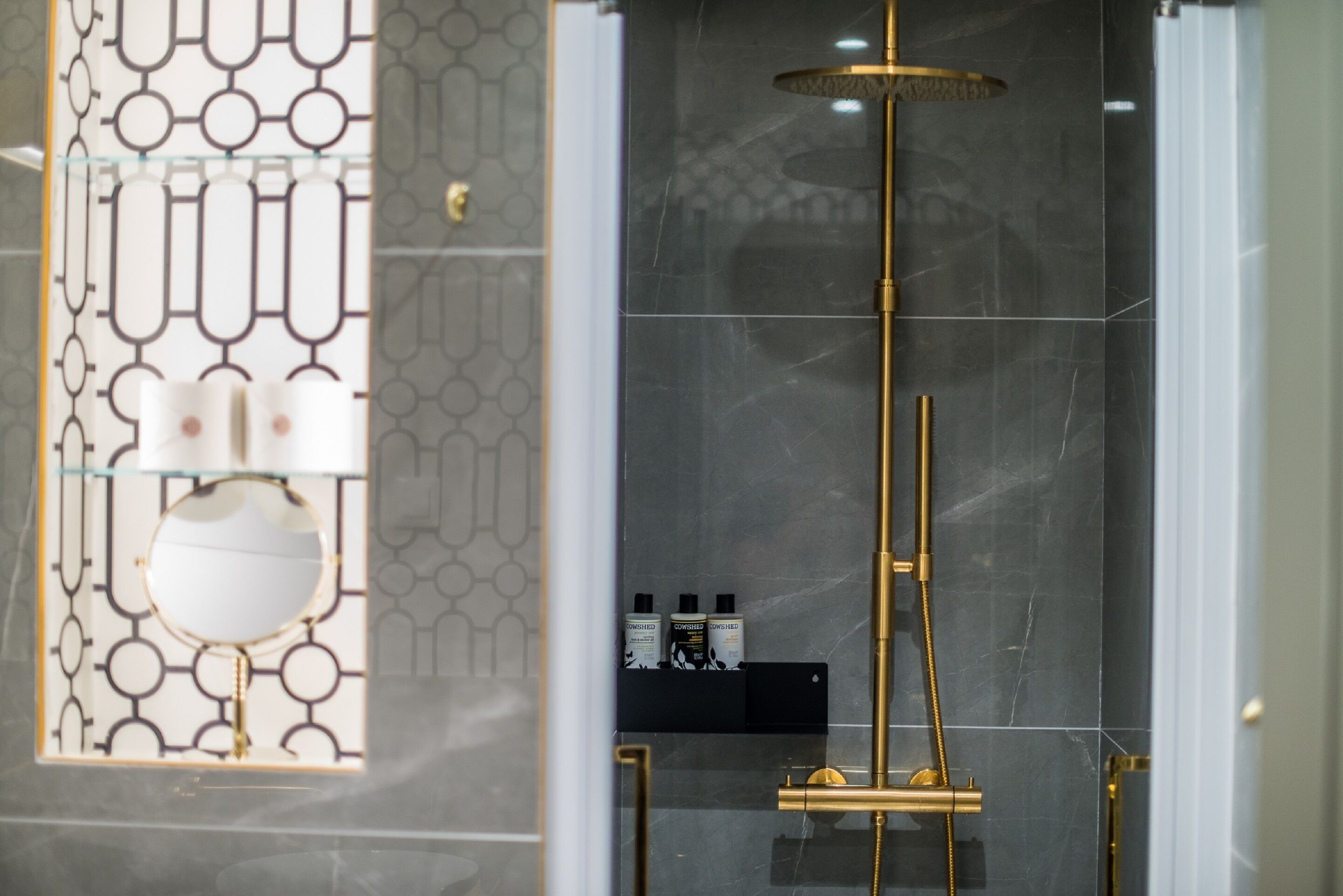 A modern bathroom with a glass enclosure, a gold showerhead, and a marble wall.
