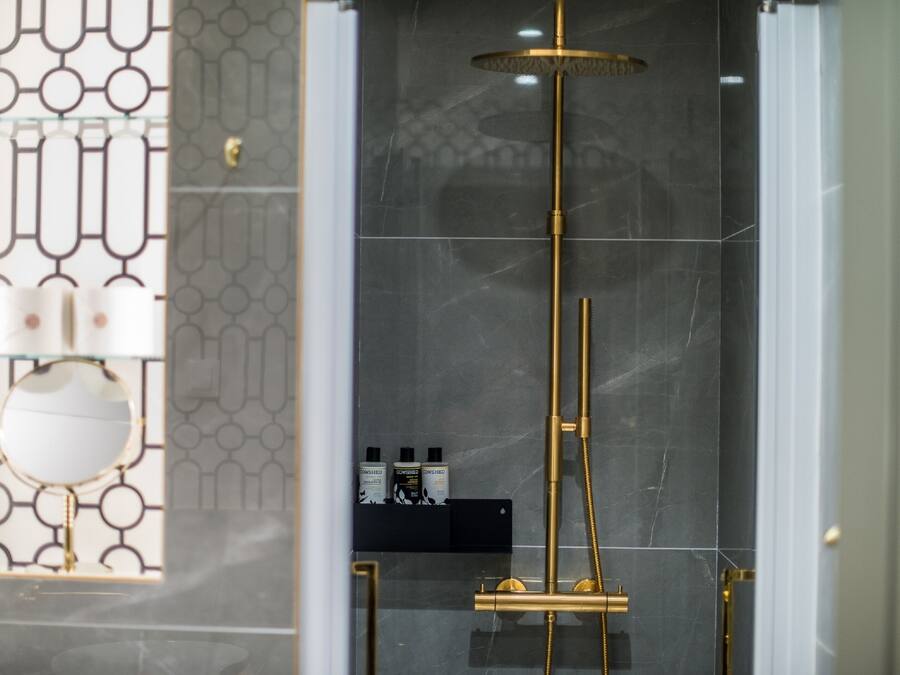 A modern bathroom with a glass enclosure, a gold showerhead, and a marble wall.
