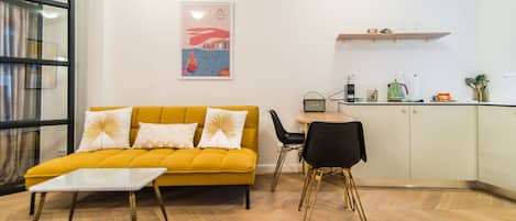 Una sala de estar moderna con un sofá amarillo, una mesita y una zona de cocina con una mesa de comedor y sillas.