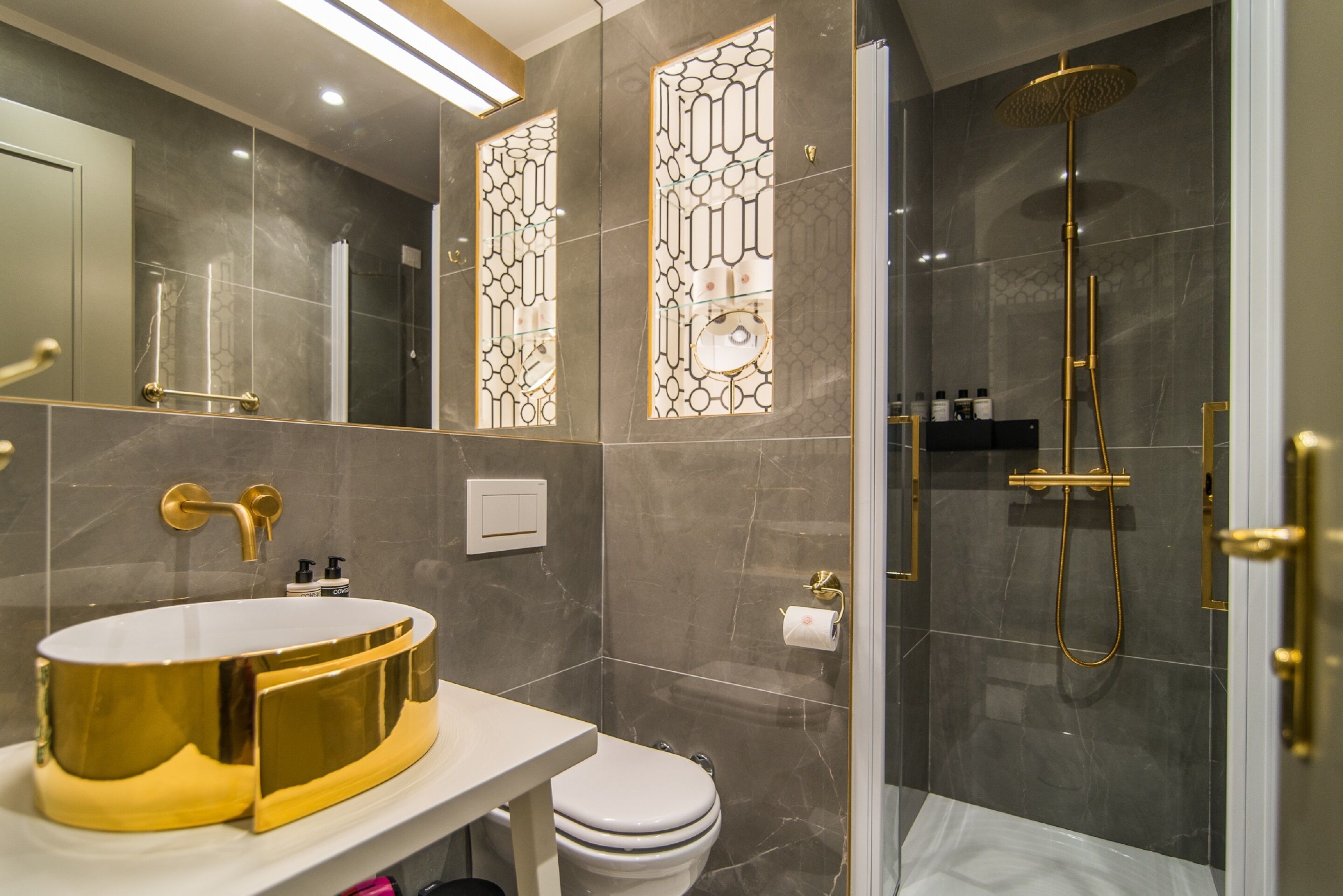 Un bagno moderno con una toeletta dorata, un water e una doccia a filo pavimento.
