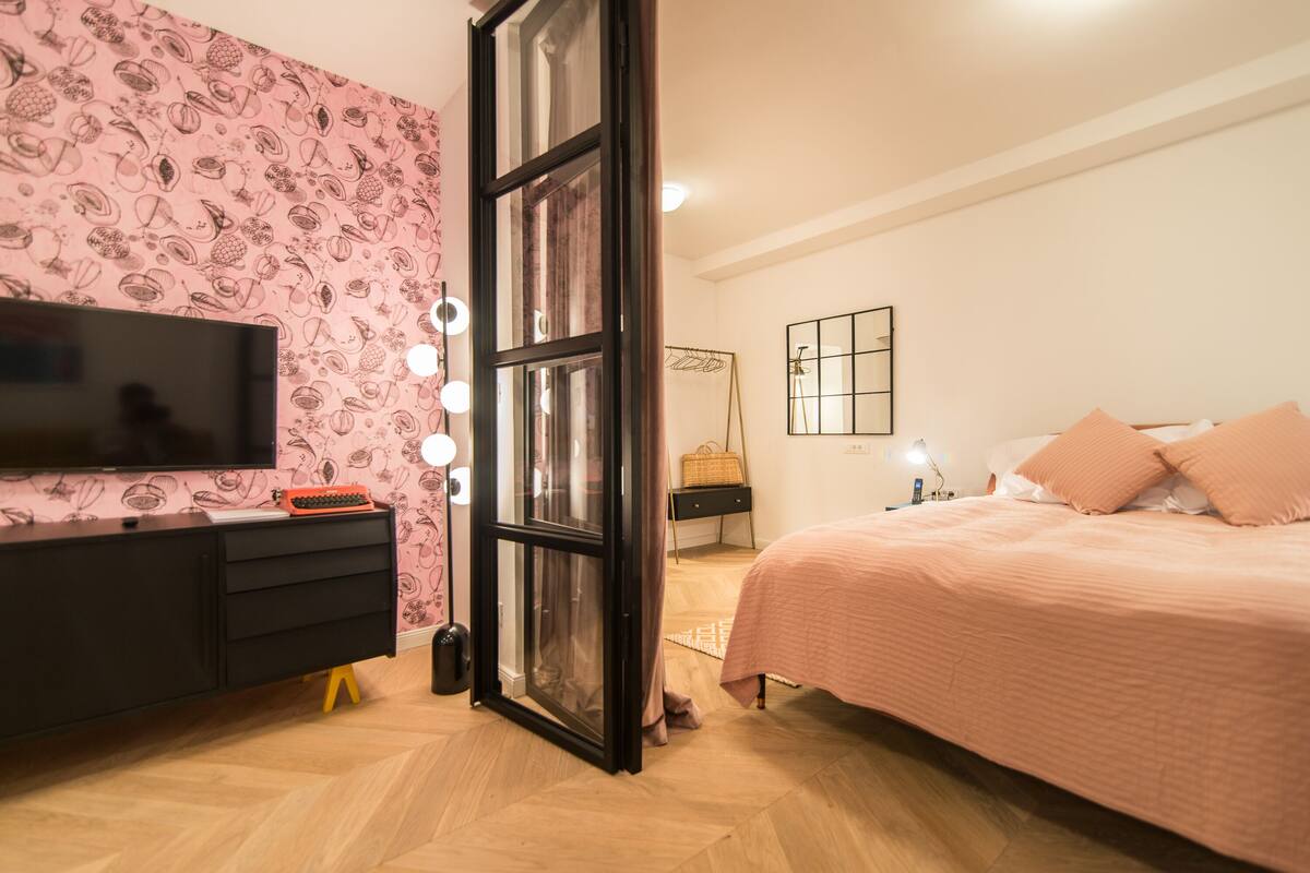 A bedroom with a bed, a dresser, a TV, and a window with curtains.
