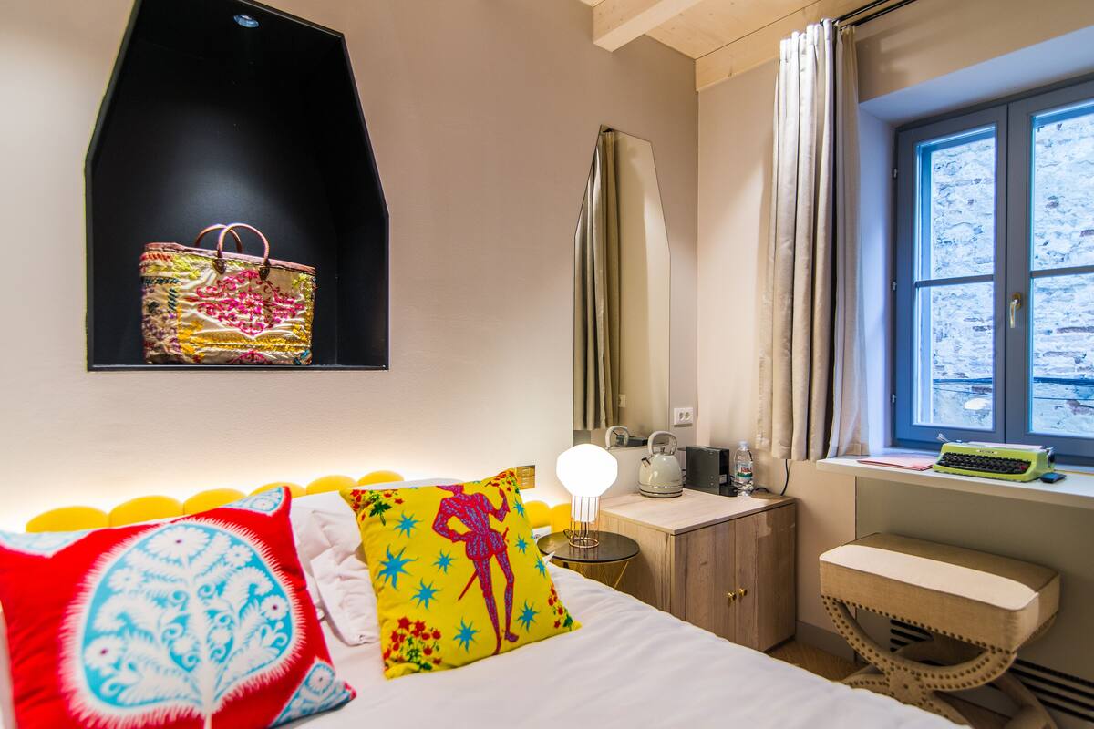 A hotel room with a bed, bedside table, lamp, and a window with a view.