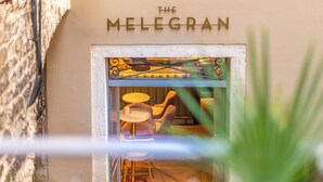 A view of The Melegran's entrance with a stone wall, a glass door, and a seating area inside. - The Melegran (Rovinj)