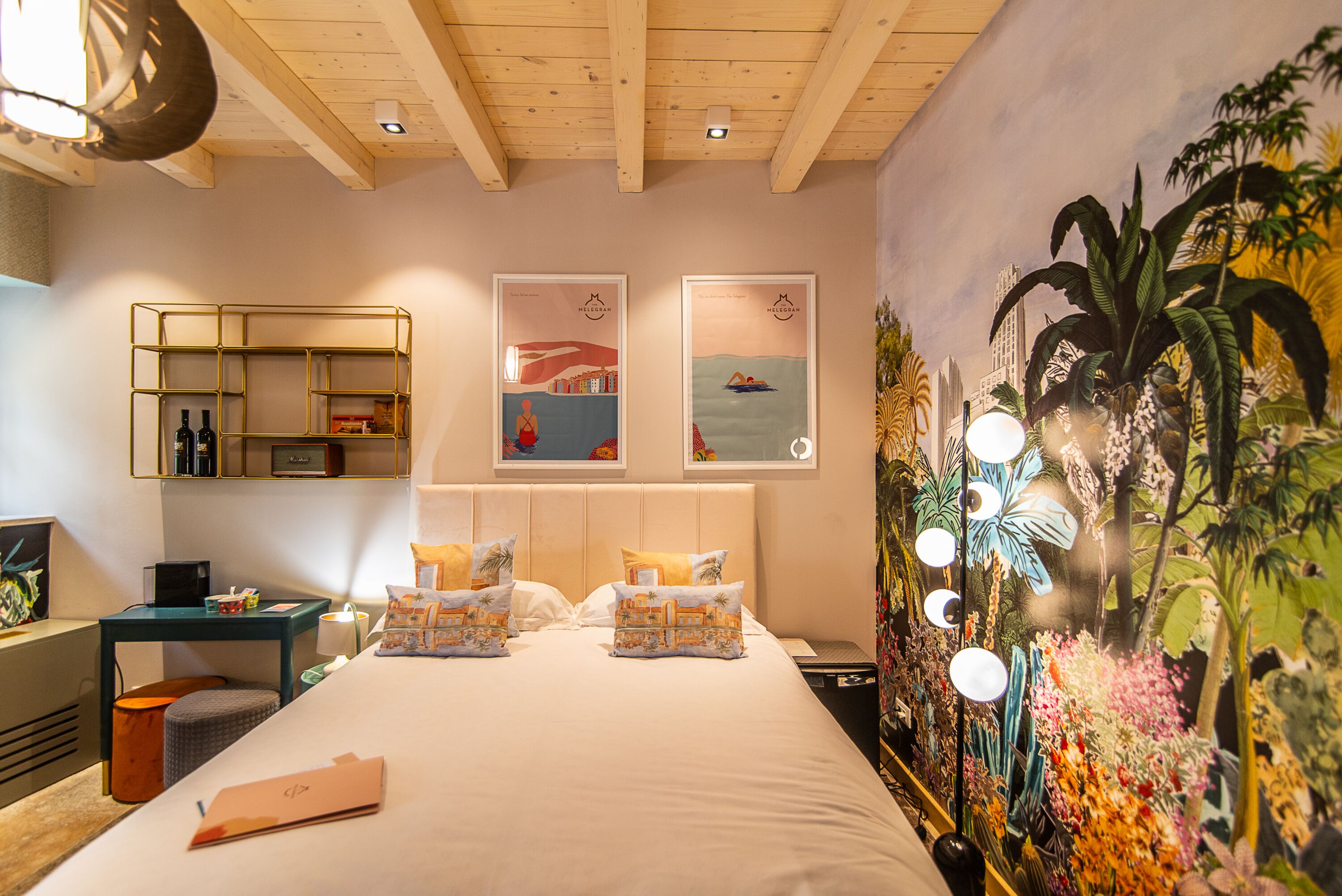 Habitación de hotel con cama, escritorio, silla, mesita de noche y una pared con un mural.