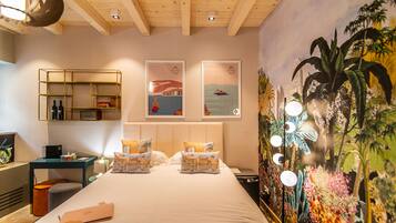 Habitación de hotel con cama, escritorio, silla, mesita de noche y una pared con un mural.