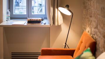 A room with a window, a desk with a typewriter, a lamp, and an orange chair.