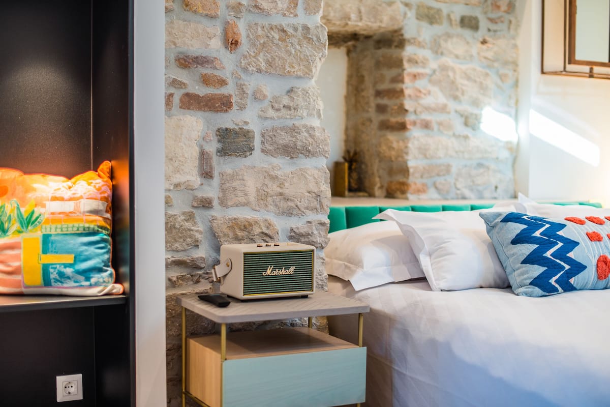 A bed with white and blue pillows, a Marshall radio on a bedside table, and a stone wall in the background.