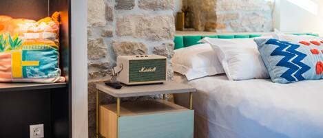 A bed with white and blue pillows, a Marshall radio on a bedside table, and a stone wall in the background.
