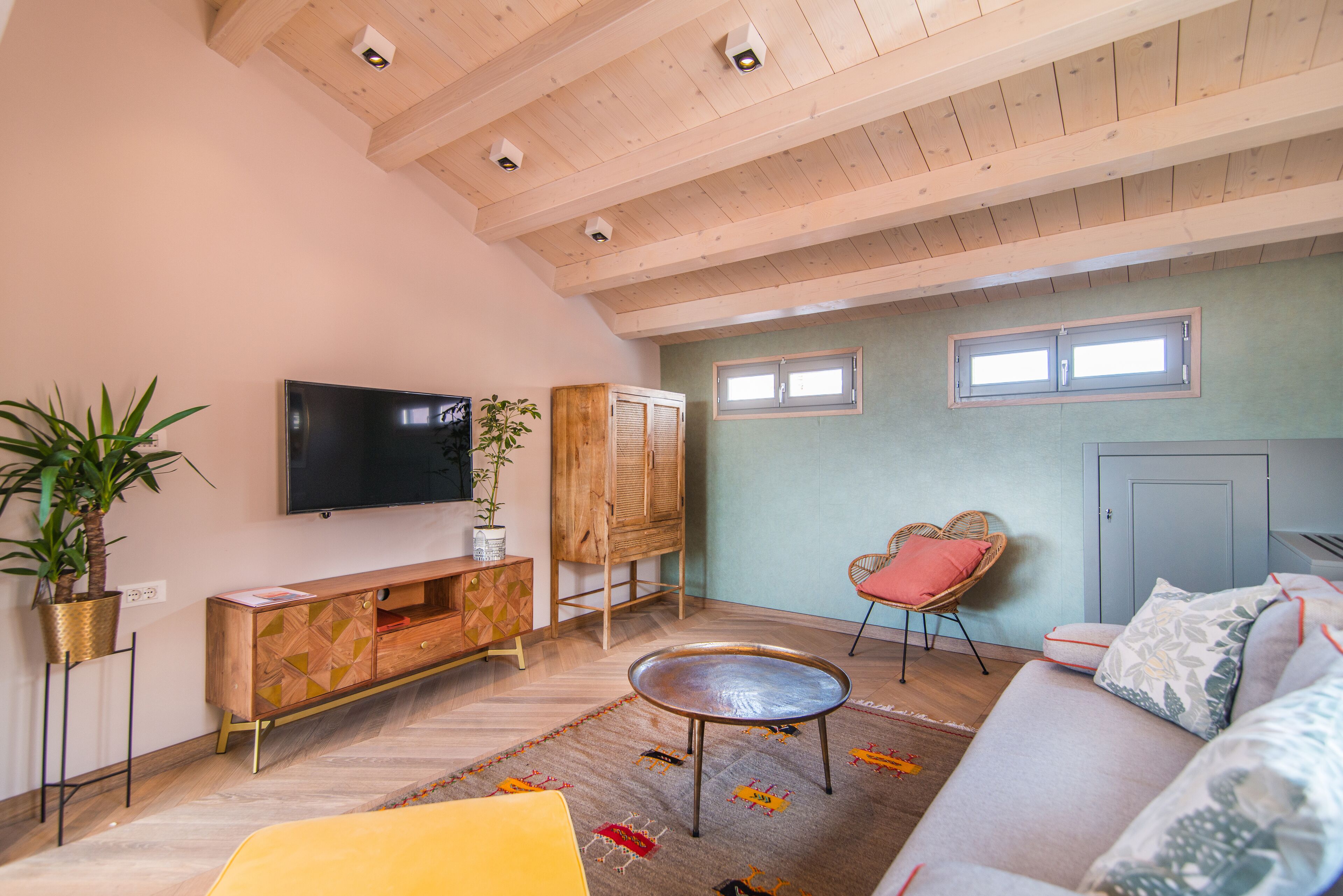 A living room with a sofa, a television, a wooden cabinet, a wicker chair, and a potted plant.