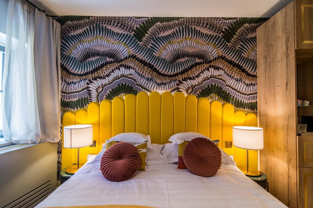 A hotel room with a yellow headboard, white bedding, and two lamps on either side.