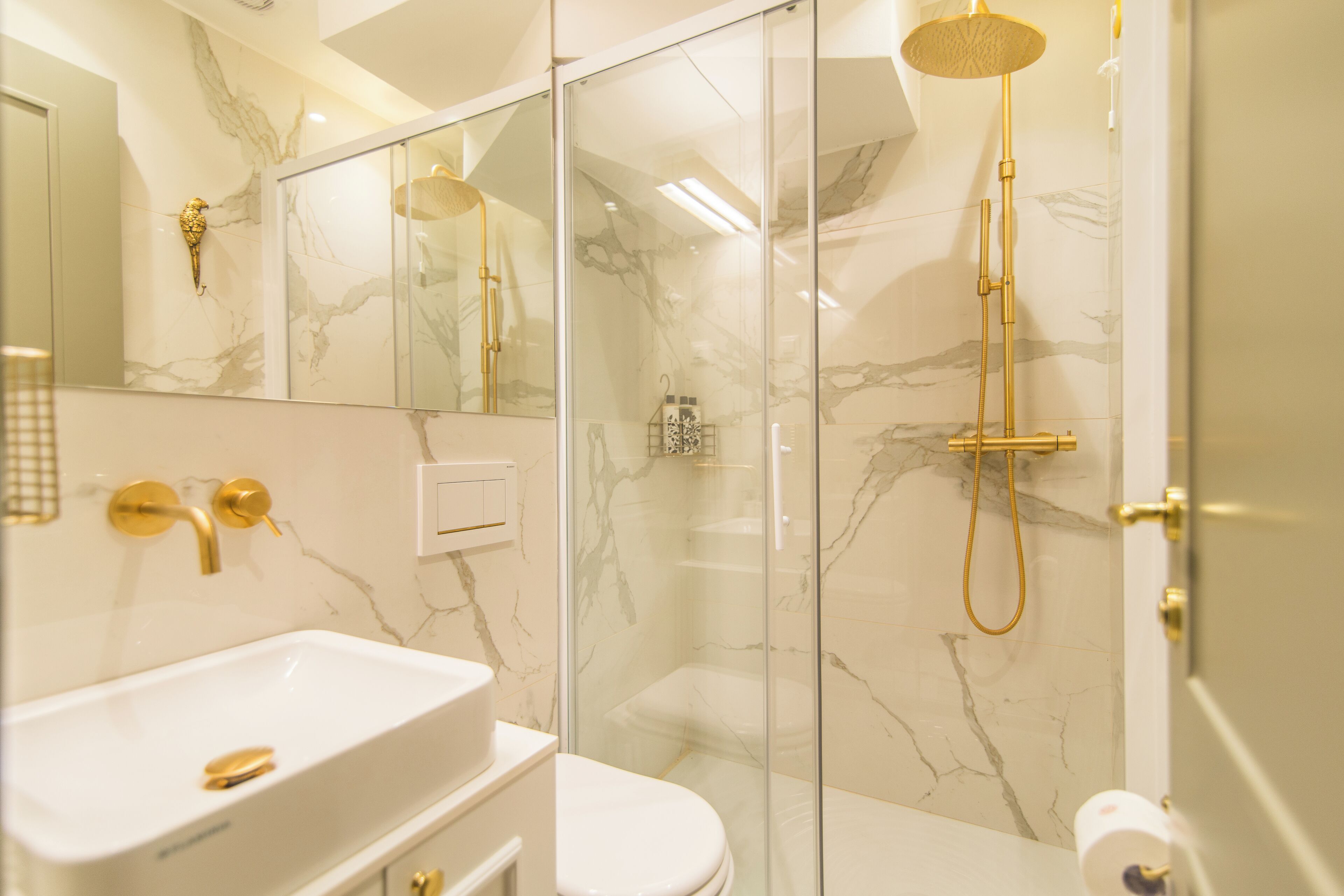 A modern bathroom with a glass-enclosed shower, a white sink with gold fixtures, and a marble backsplash.