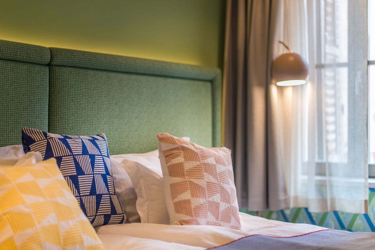 A neatly made bed with patterned pillows, a green headboard, and a window with curtains.