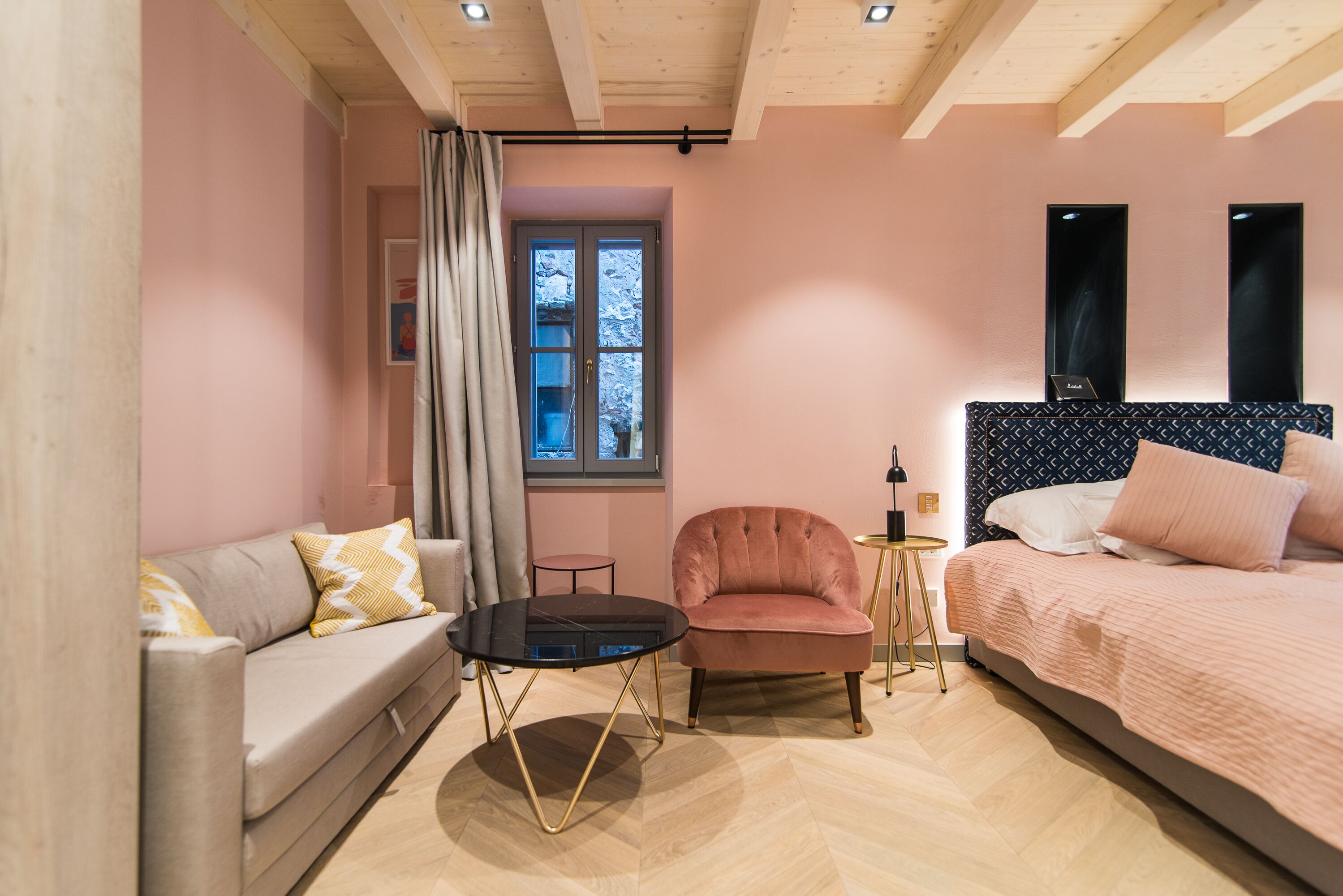 A cozy room with a sofa, a chair, a small round table, a bed, and a window with a view.
