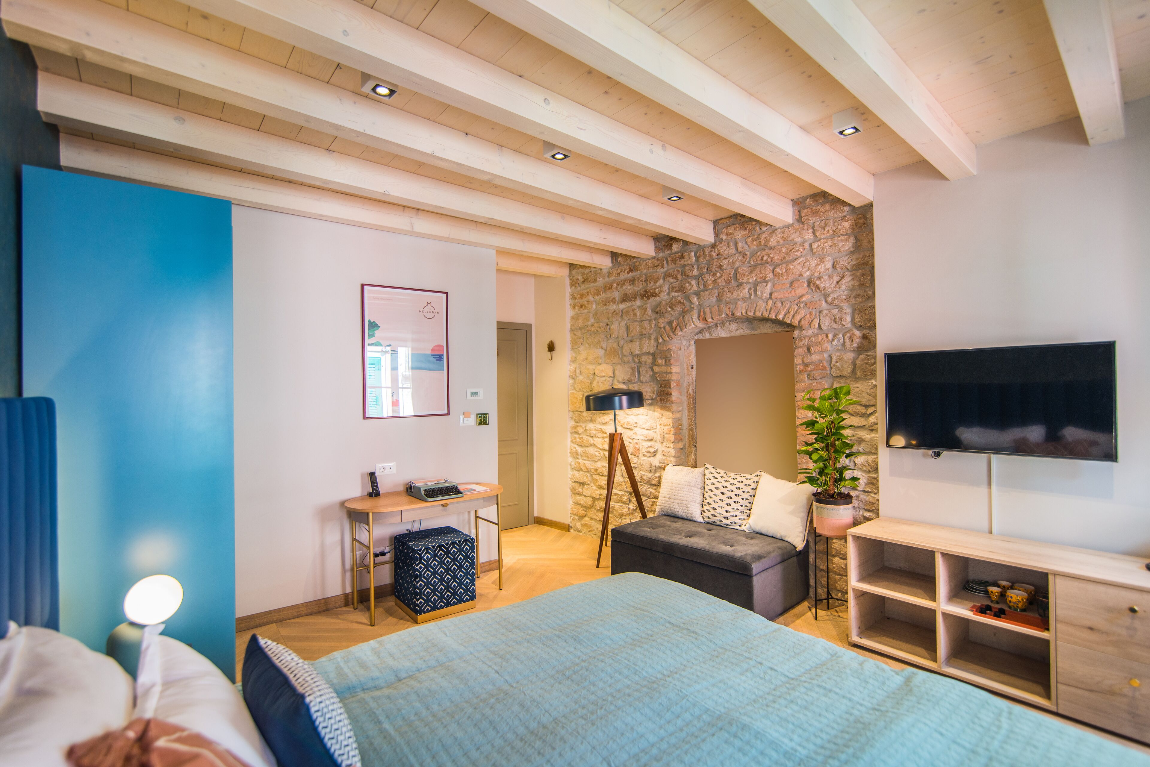 Une chambre à coucher avec un lit, un bureau, une télévision et un mur en pierre.