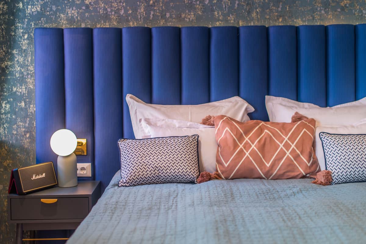 A neatly made bed with patterned pillows, a bedside lamp, and a Marshall speaker on a nightstand.