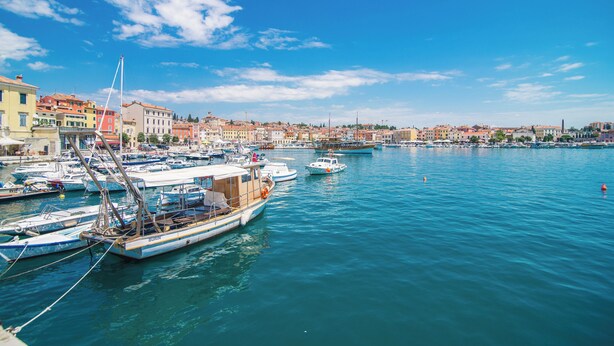 A harbor with boats docked, buildings along the waterfront, and a clear blue sky. - The Melegran (Rovinj)