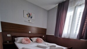 A hotel room with a large bed, a wooden headboard, a small bedside table, and a window with curtains.