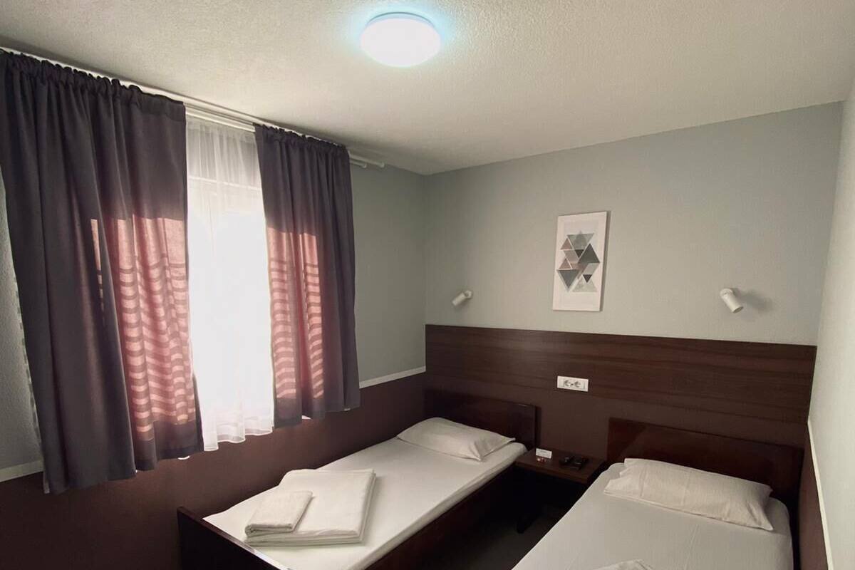 Una habitación con dos camas individuales, una ventana con cortinas, una lámpara en el techo y un cuadro enmarcado en la pared.