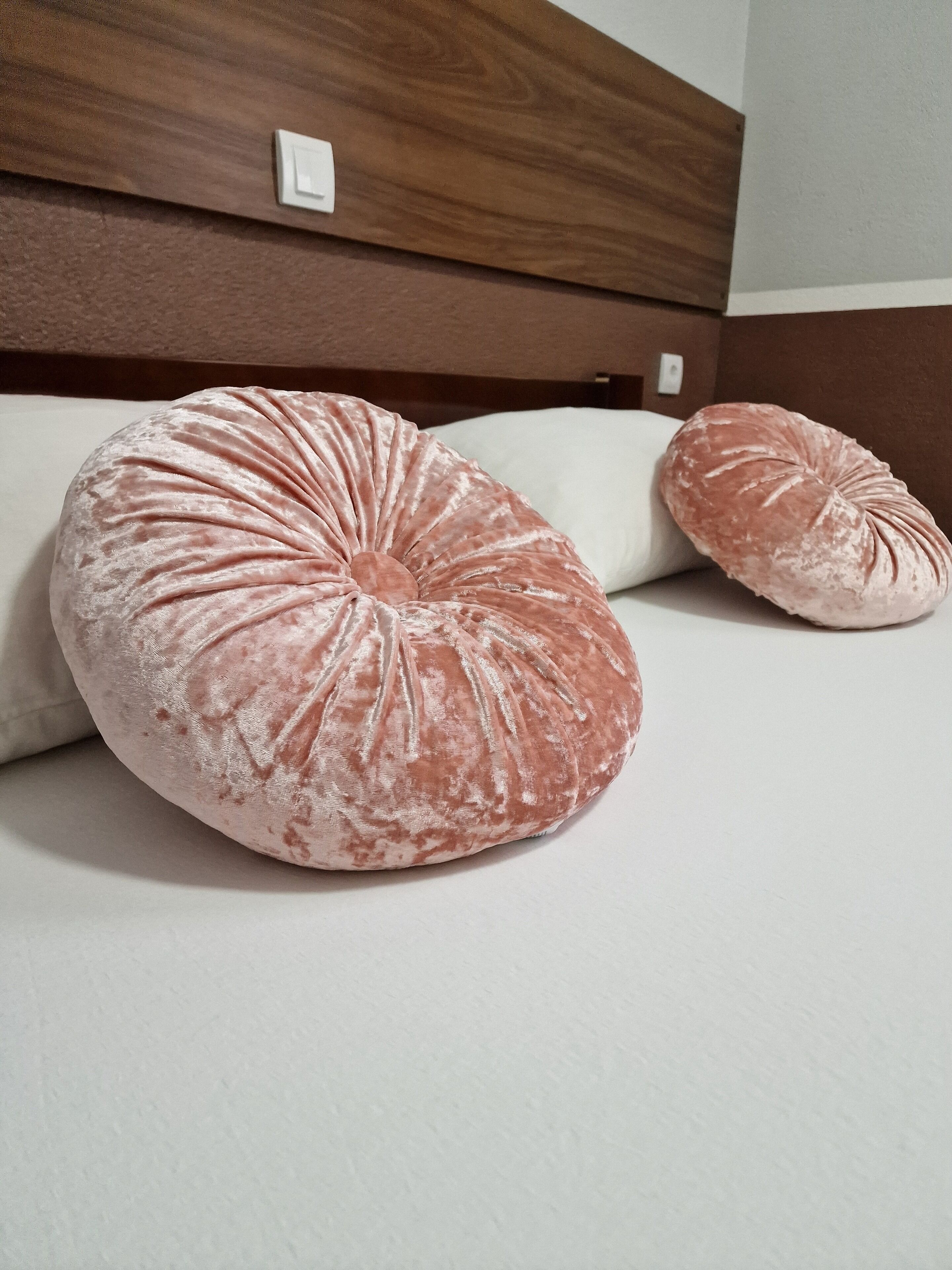 Un lit avec deux grands oreillers ronds de couleur rose et une tête de lit en bois.