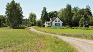 A house with a white exterior and a sloped roof, surrounded by a green field and trees. - Beautiful home in Säffle with kitchen (Säffle)