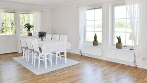 A bright dining room with a white table and chairs, large windows with curtains, and a wooden floor. - Beautiful home in Säffle with kitchen (Säffle)