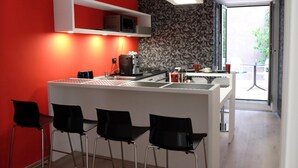 Una cocina moderna con una pared roja de acento, una isla blanca con taburetes y vistas al exterior a través de un ventanal.