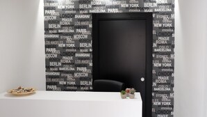Una habitación con una puerta negra, un mostrador de recepción blanco y una pared decorada con nombres de ciudades.