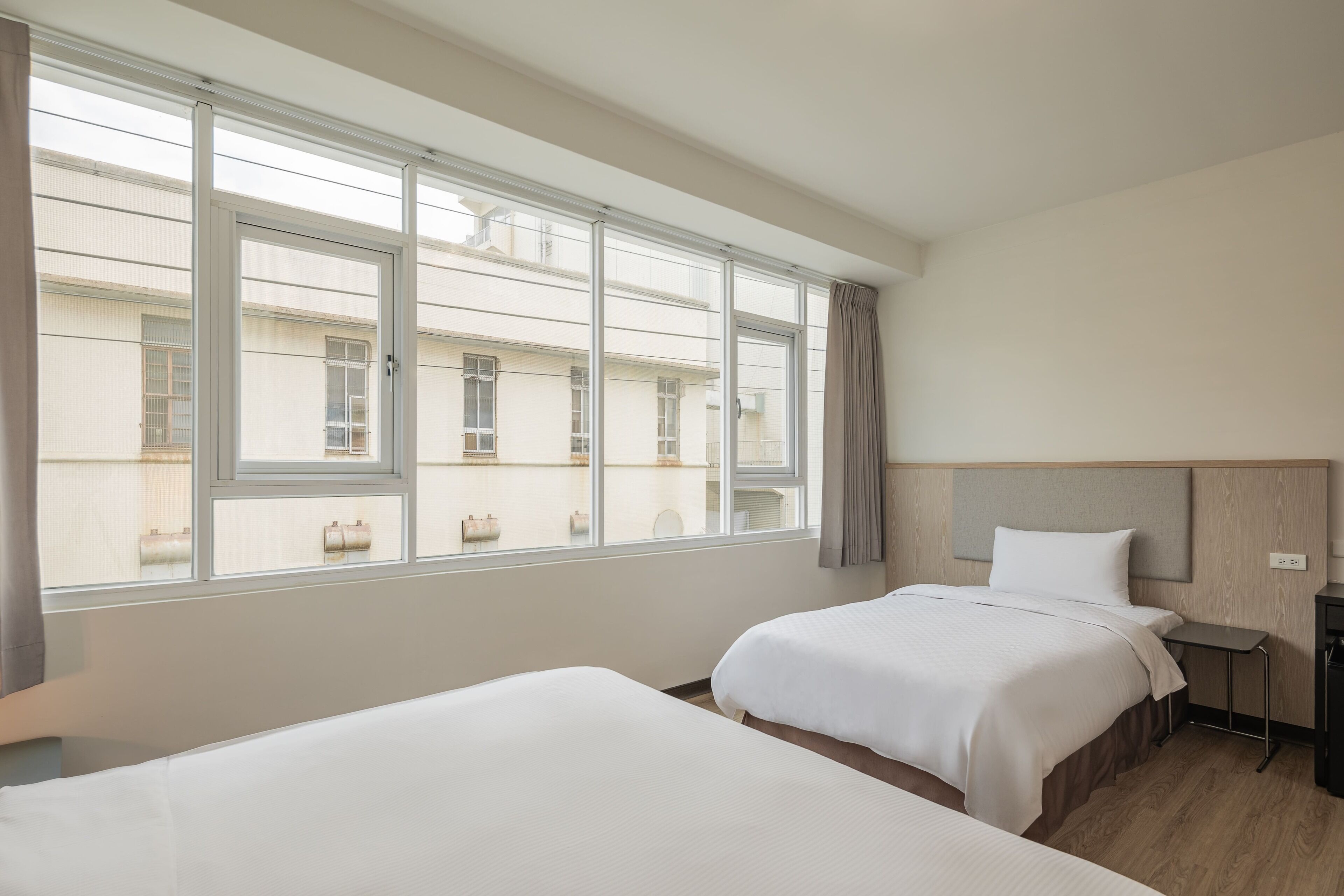 Une chambre d’hôtel avec deux lits, une petite table et une vue sur les bâtiments, visible à travers de grandes fenêtres.