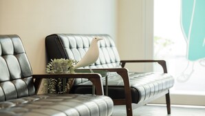 A modern living room with leather sofas, a small table with a decorative bird and plants, and a view of a green outdoor area. - Meant to Be (Chiayi City)