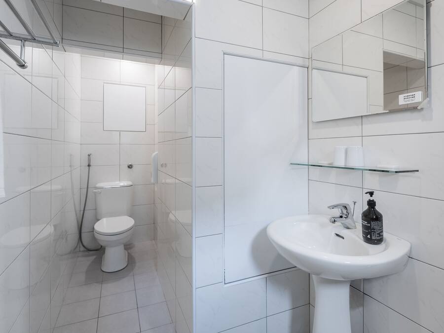 Un baño moderno con azulejos blancos, un lavamanos blanco, una repisa de vidrio y un inodoro.