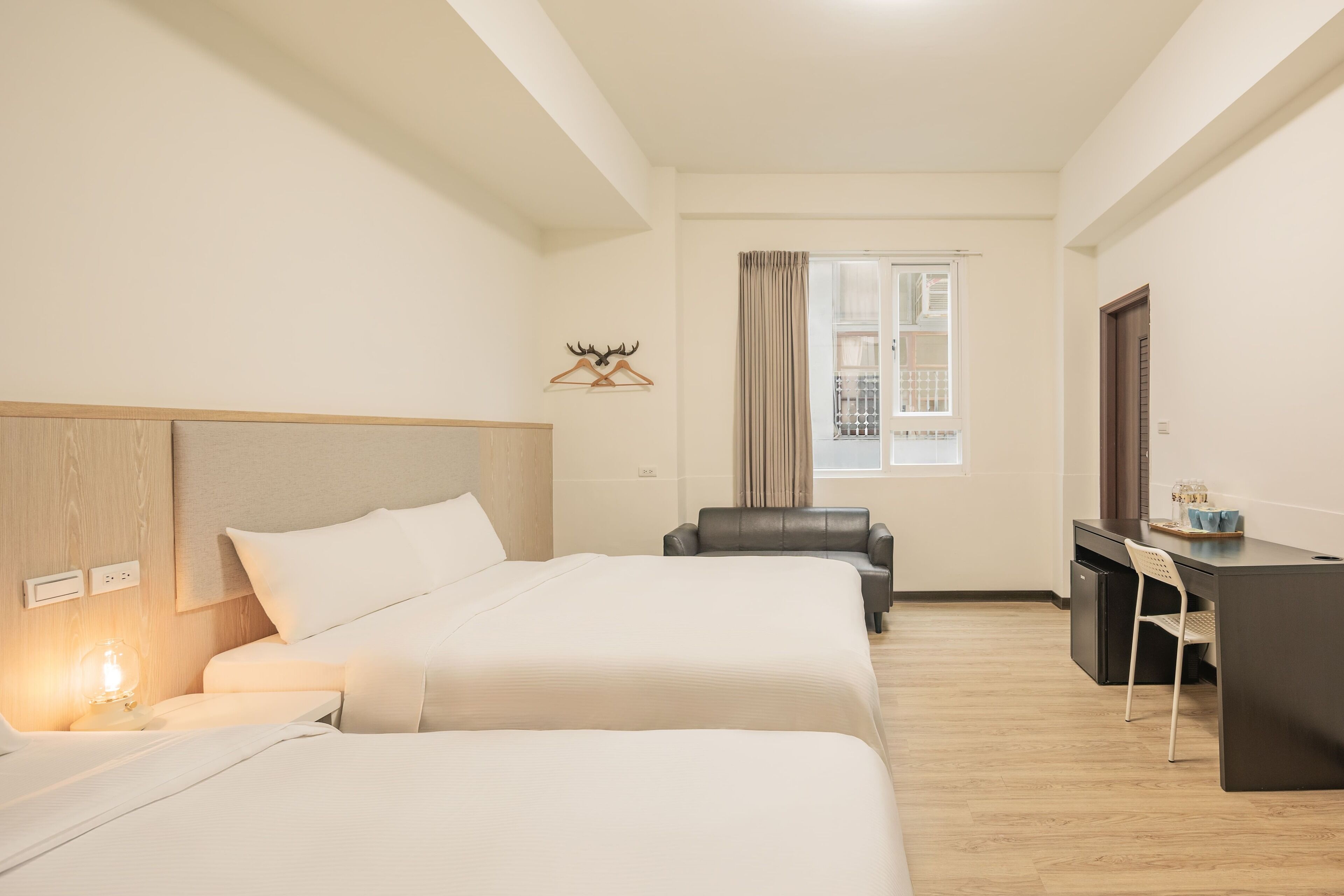 Habitación de hotel con dos camas, un escritorio, una silla, una lámpara, un perchero con cabeza de venado y una ventana con cortinas.