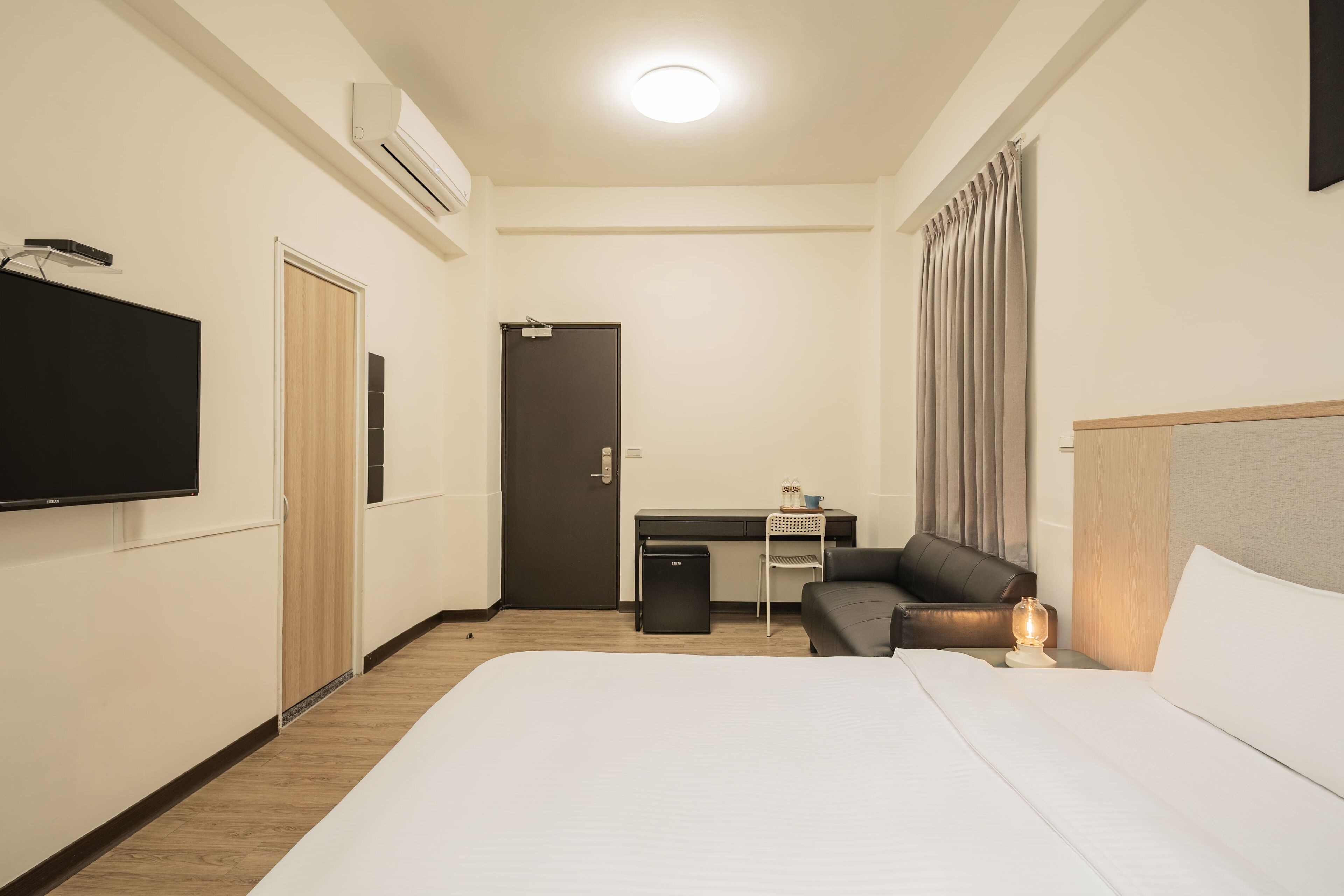 Una camera d'albergo con un letto, una scrivania, una sedia, una televisione e un comodino con una lampada.