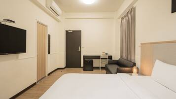Una camera d'albergo con un letto, una scrivania, una sedia, una televisione e un comodino con una lampada.