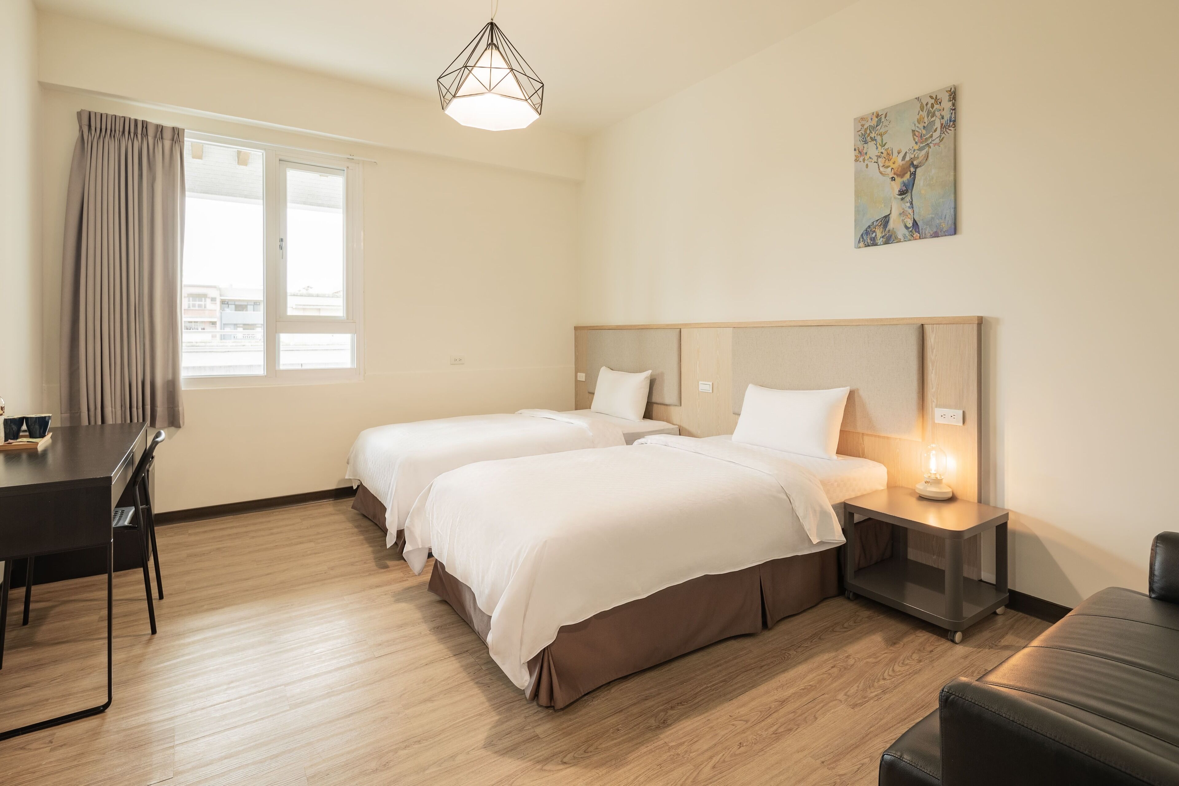 Ein Hotelzimmer mit zwei Betten, einem Schreibtisch, einem Stuhl, einer Lampe und einem Bild an der Wand.