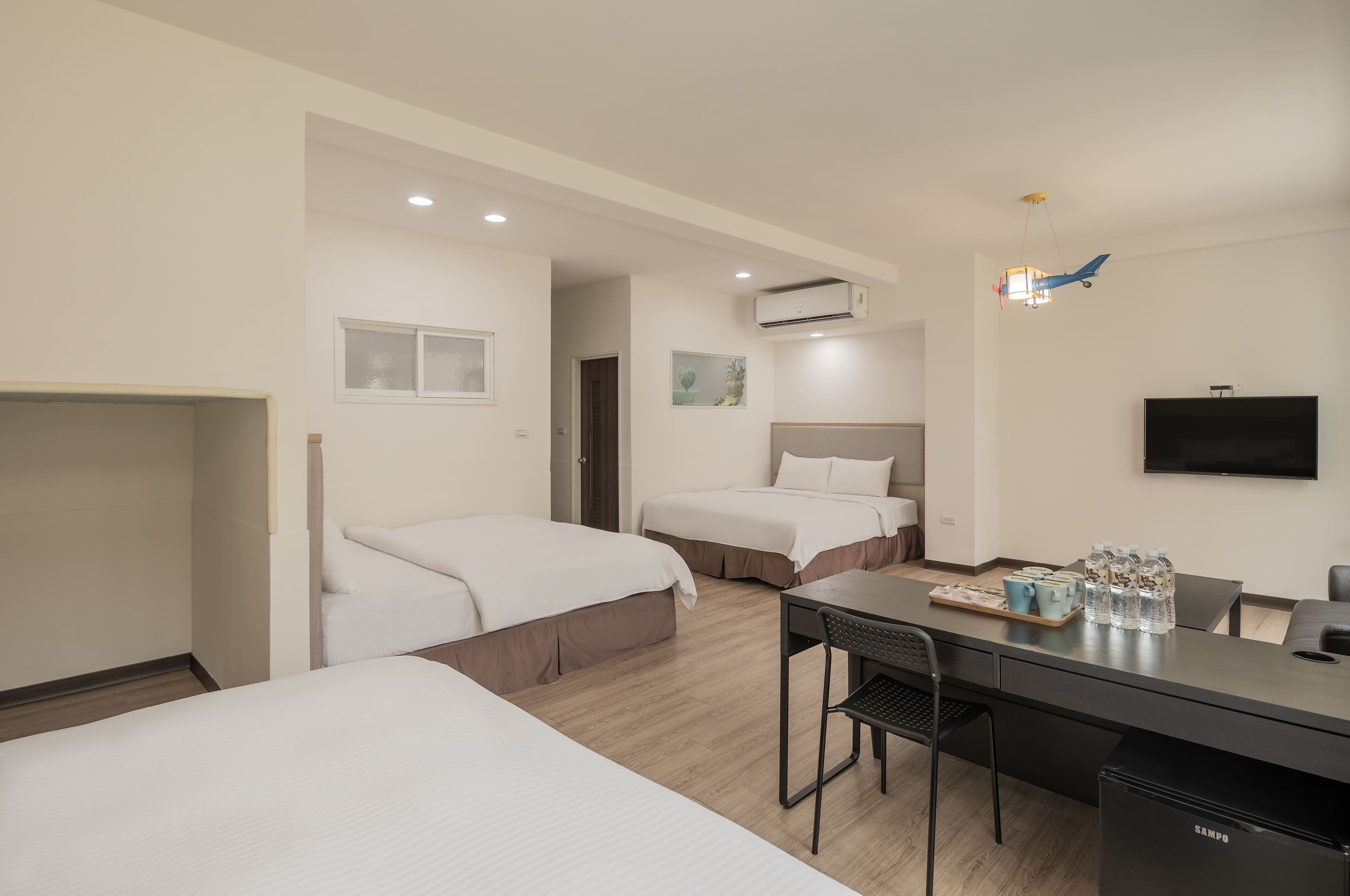A hotel room with two beds, a desk with a chair, a television, and a minibar.