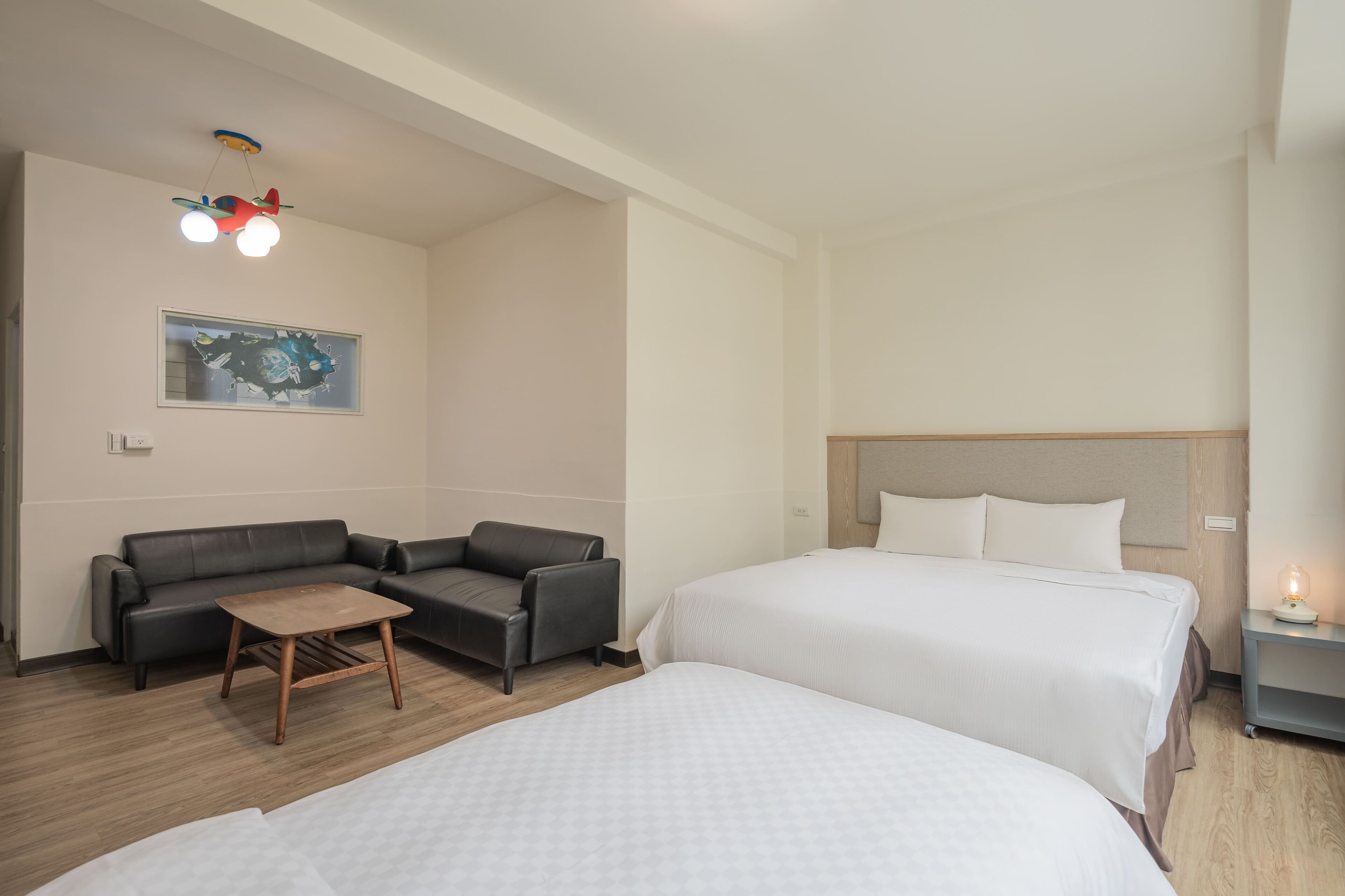A hotel room with two beds, a sofa, a small wooden table, and a ceiling light fixture.