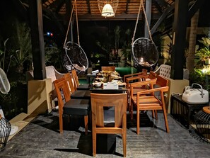 An outdoor dining area with a table set for six, surrounded by wooden chairs and two hanging chairs. - Montra Samui (Koh Samui)
