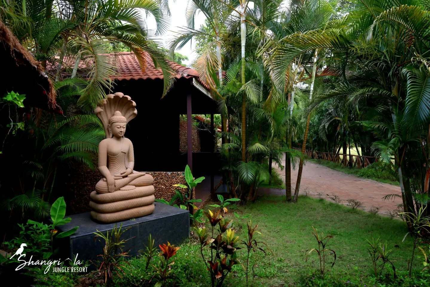 Una estatua de Buda en un jardín con un edificio rústico y un sendero.