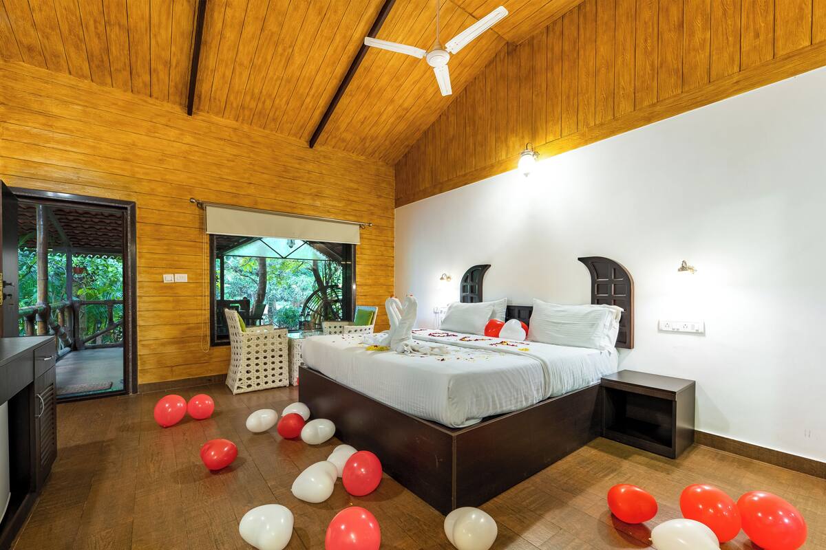 A room with a wooden ceiling, a bed with white bedding, and a view of greenery through a window.