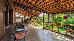 Una terraza cubierta de madera con mobiliario de mimbre y barandilla de bambú, con vistas a un jardín exuberante.