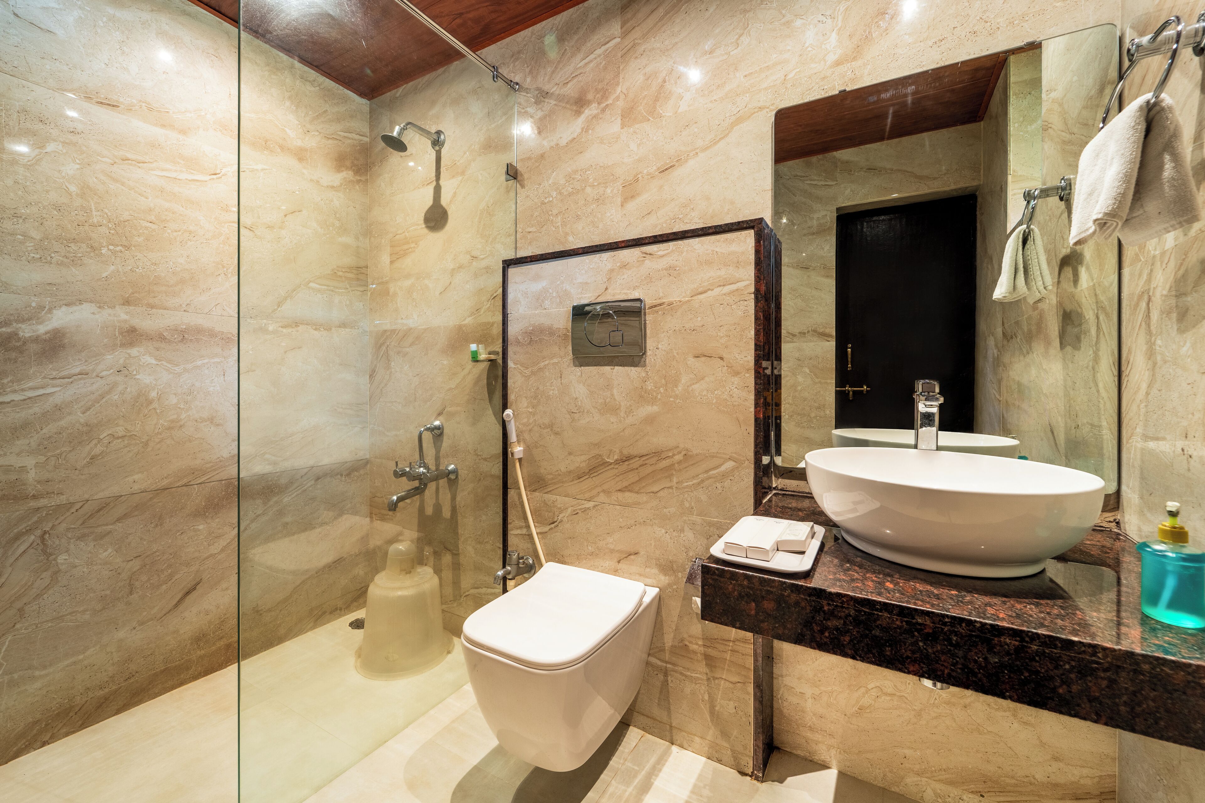 A modern bathroom with a glass-enclosed shower, a white toilet, a marble-tiled wall, and a large mirror above a sink with a marble countertop.