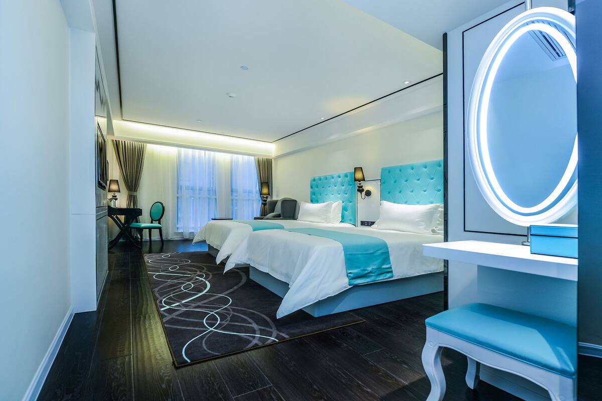 Ein modernes Hotelzimmer mit einem großen Bett, einem Nachttisch, einem Sessel, einem Schreibtisch und einem großen Spiegel.