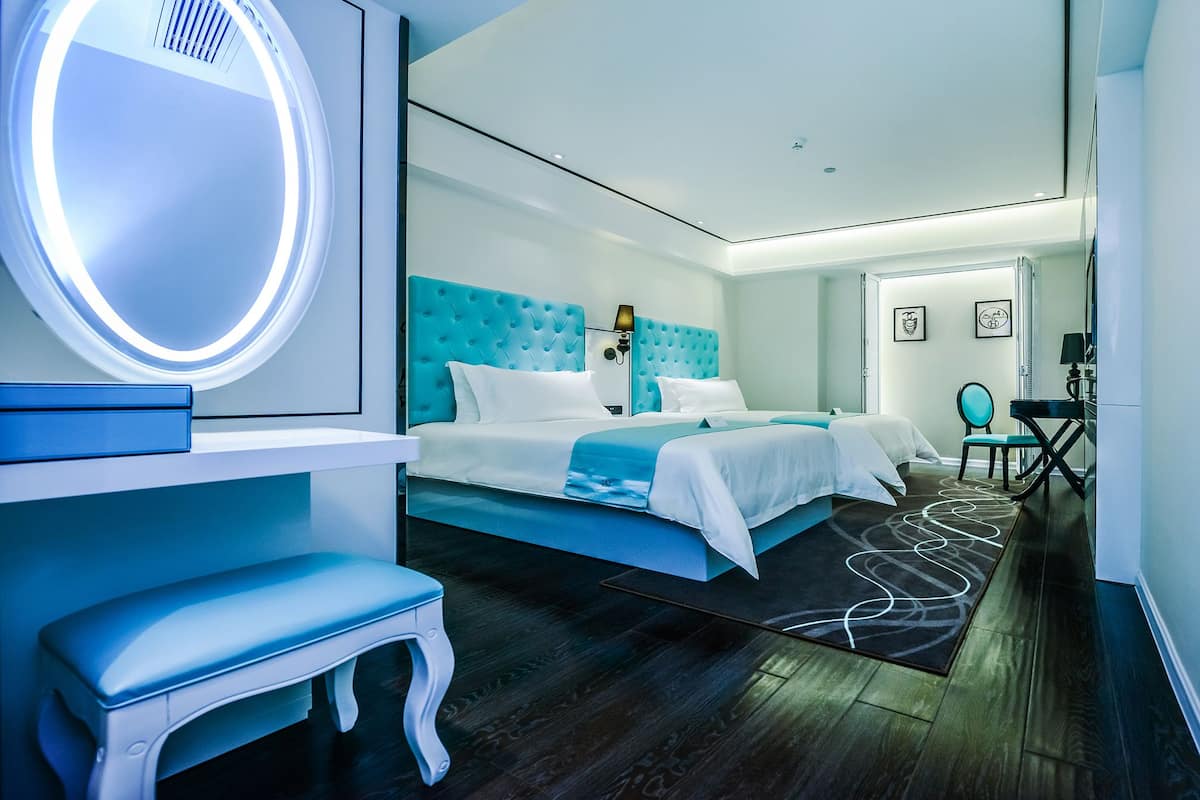 Ein modernes Hotelzimmer mit einem großen Bett, einem Schminktisch mit Spiegel, einer Bank und einem Schreibtisch.