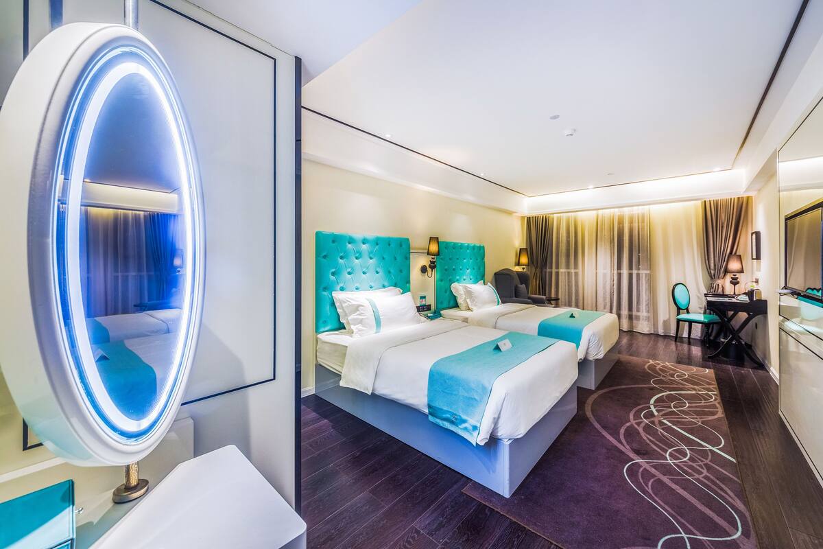 Ein modernes Hotelzimmer mit zwei Betten, einem großen Spiegel mit Beleuchtung, einem Schreibtisch und einem Stuhl.